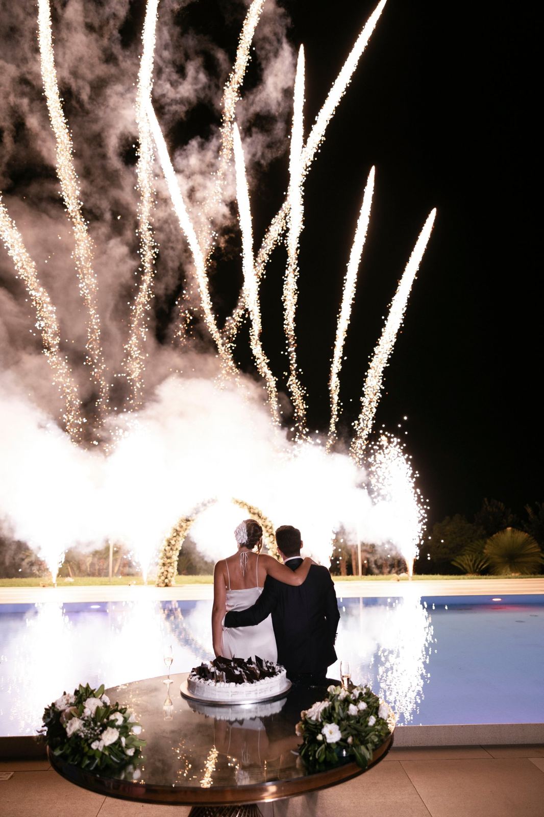 Gli sposi abbracciati guardano i fuochi d'artificio sulla piscina