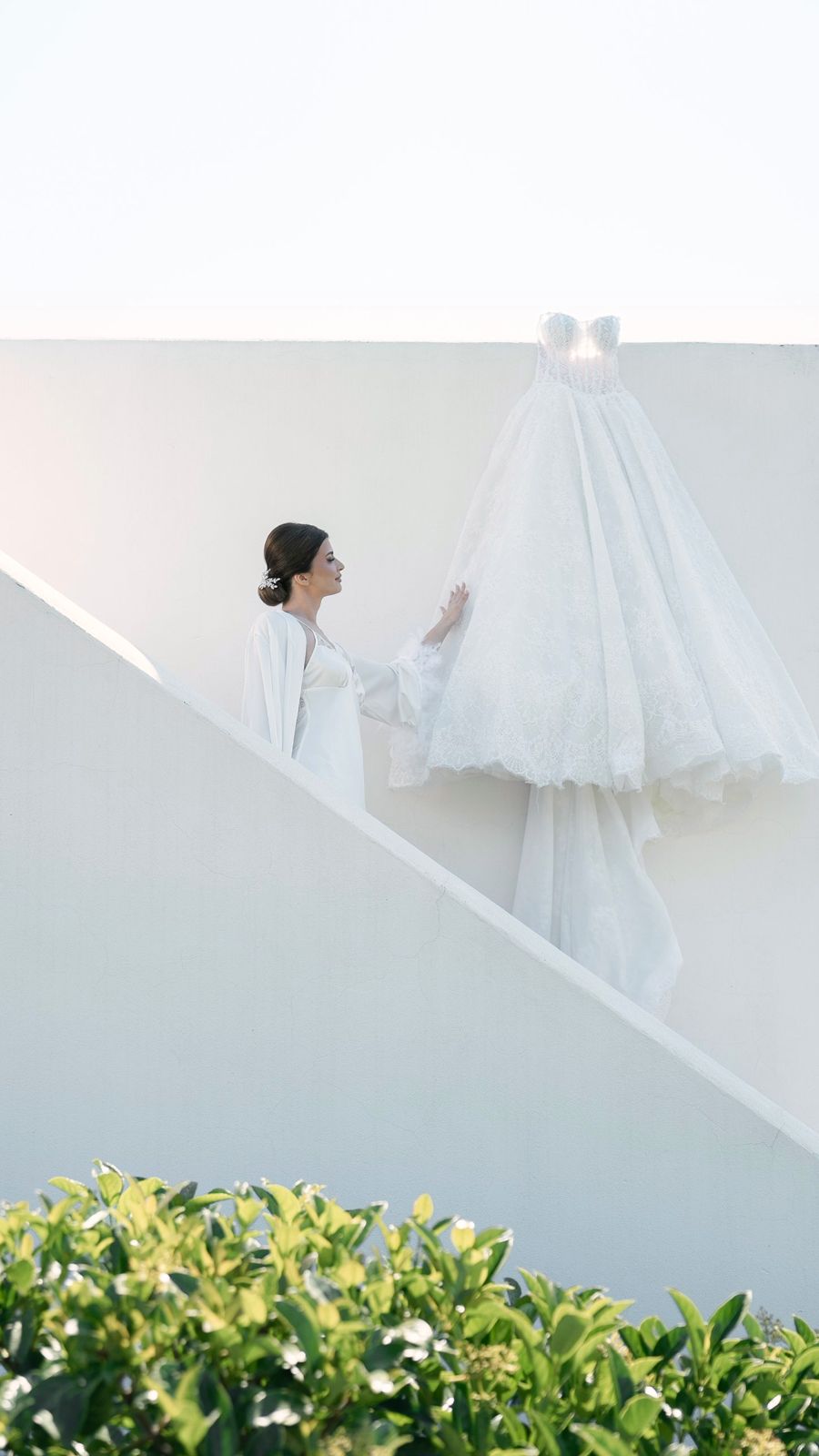 La sposa sale una scala bianca verso l'abito appeso al muro