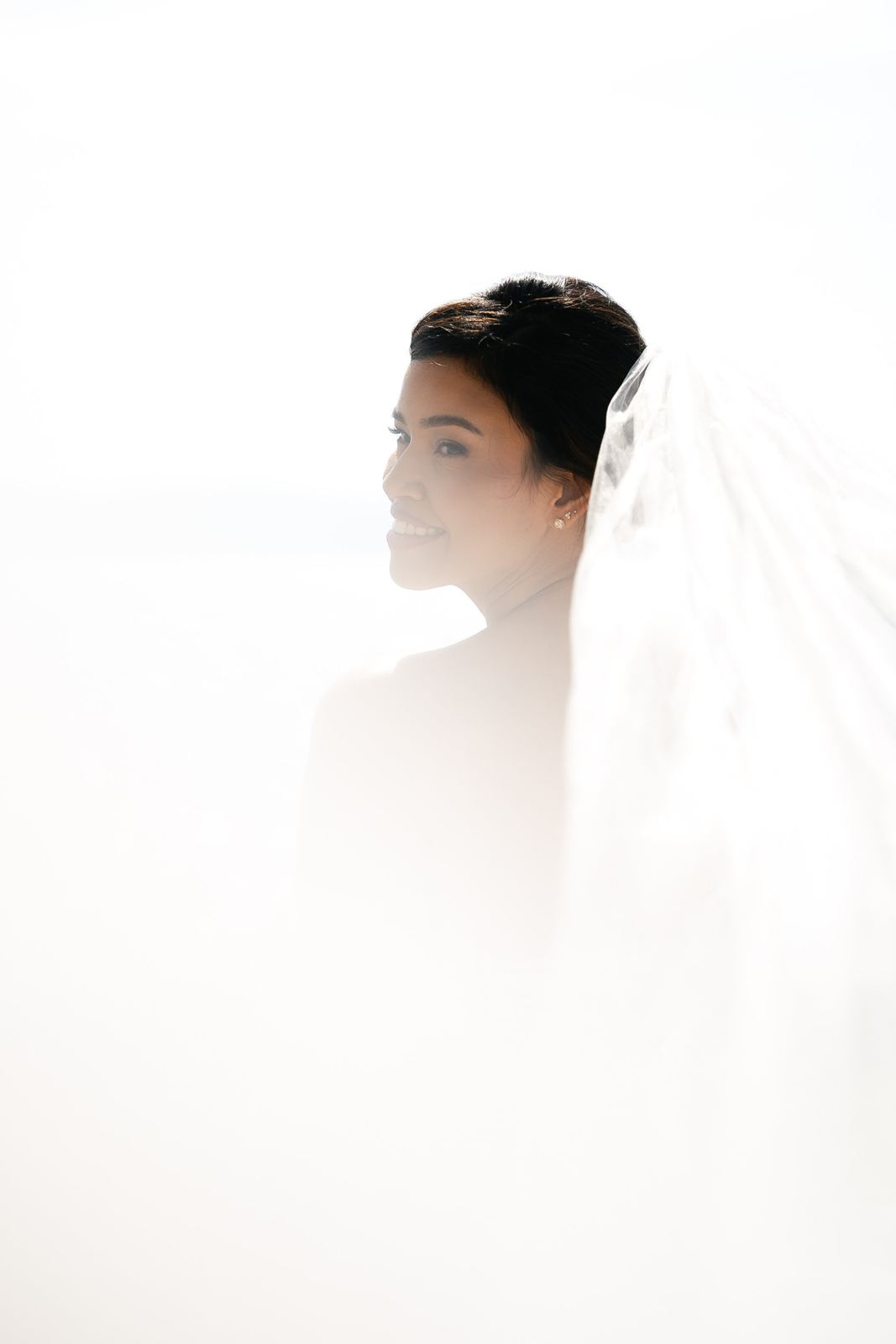 La sposa sorride avvolta nella luce bianca e nel velo