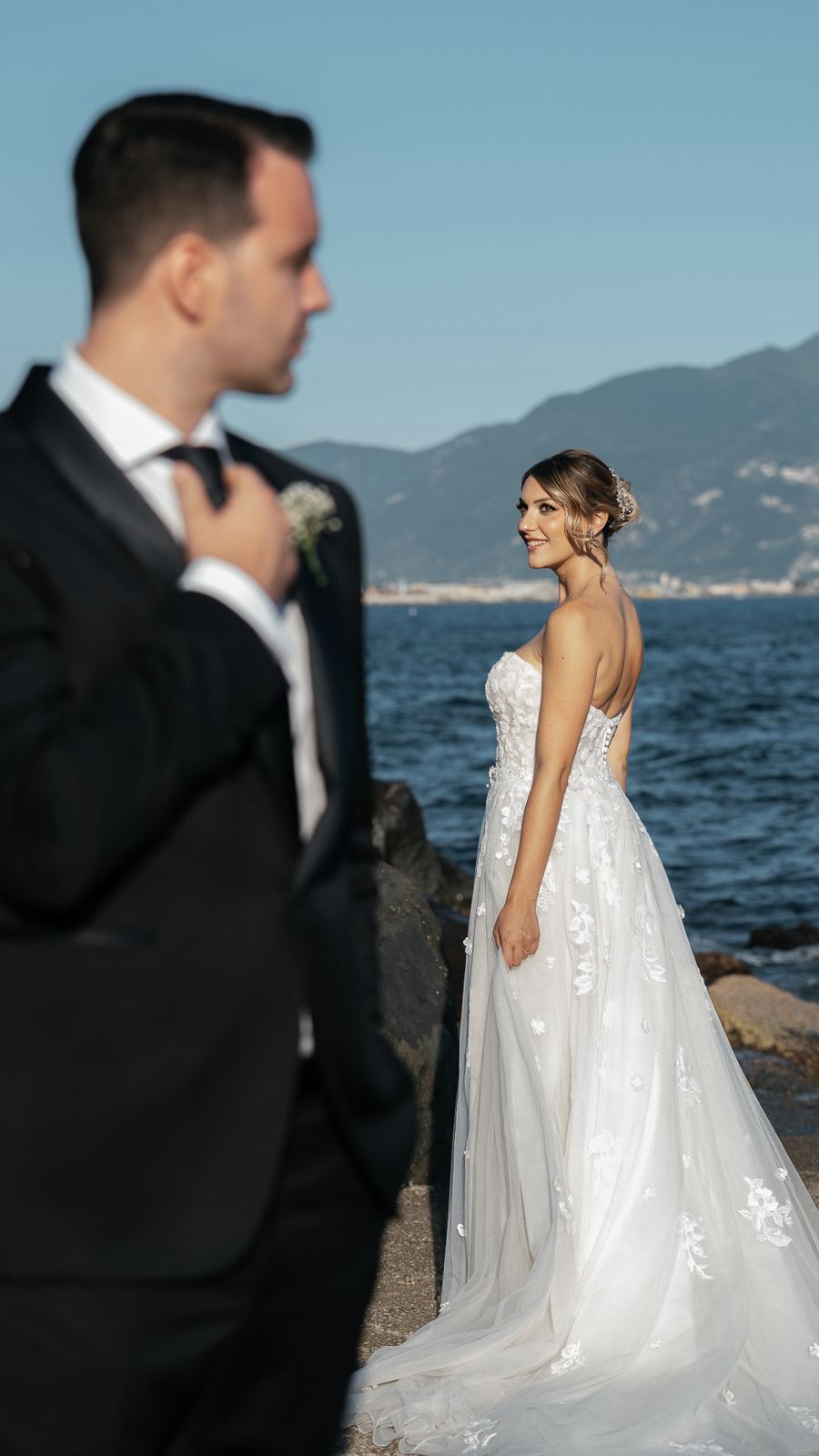 La sposa si volta verso lo sposo, sugli scogli davanti al mare