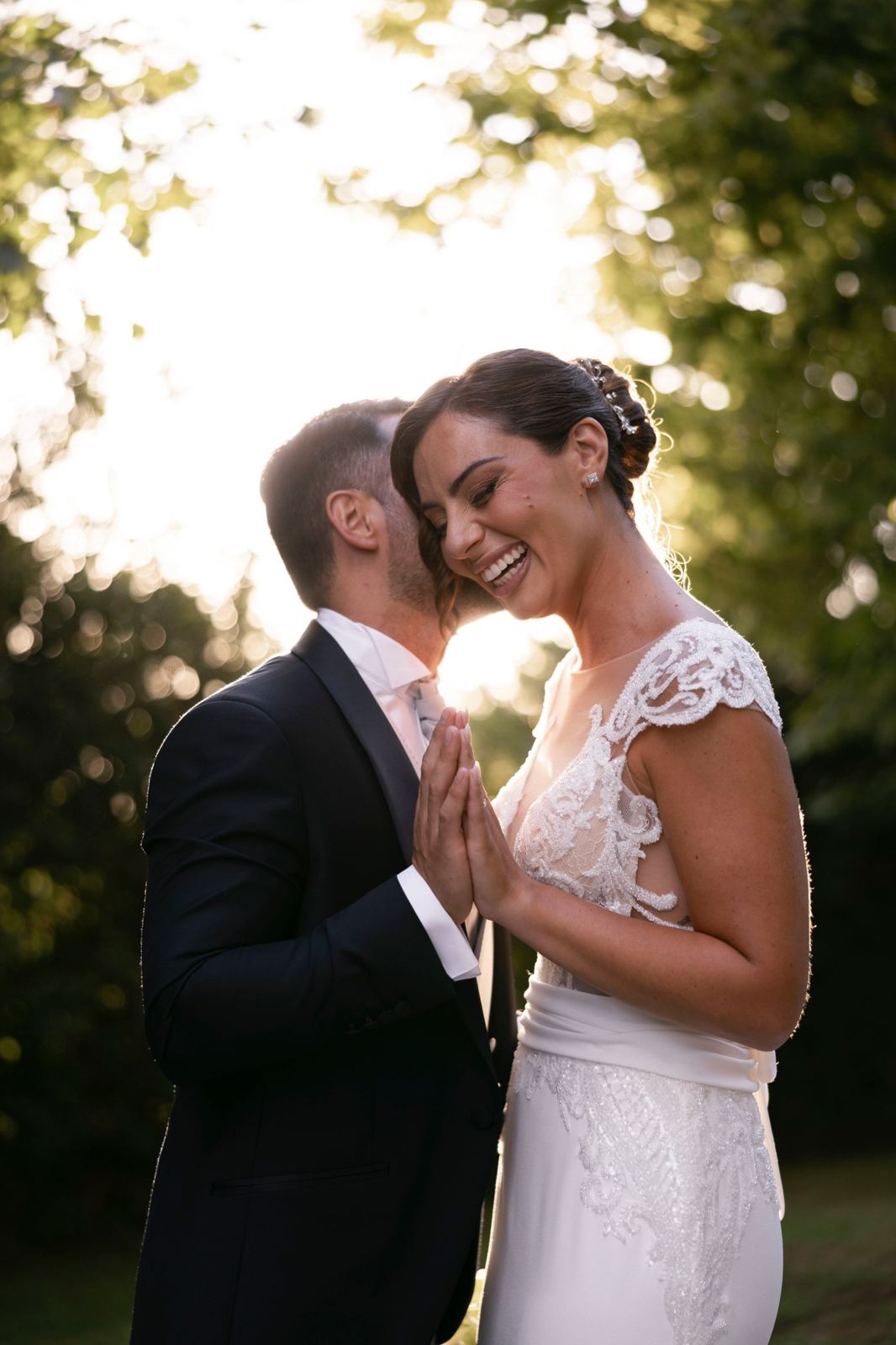 La sposa ride mentre lo sposo la bacia, controluce tra gli alberi